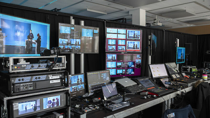 Mehrere Bildschirme, Laptops und Schaltpulte in einem Regieraum für digitale Events
